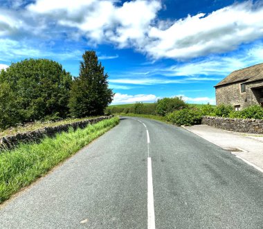 Gledstone Yolu boyunca bakın, kuru taş duvarlar, eski ağaçlar, binalar, ve mavi gökyüzü, West Marton, Skipton, İngiltere