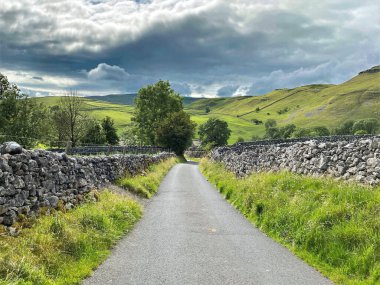 Hawthorns Yolu 'nda ilerliyoruz. Kuru taş duvarlar, çimenler ve ağır yağmur bulutlarıyla Malham, Skipton, İngiltere.