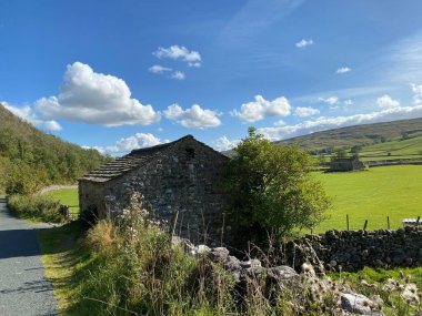 Yol kenarındaki eski taş ahır ve bir diğeri de sıcak bir yaz gününde Hawkswick, Skipton, İngiltere yakınlarındaki bir tarlada.