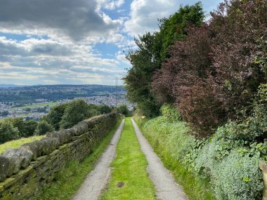Aşağıya, Pule Green Lane 'e bakıyorum, Halifax' a doğru inerken, kurumuş taş duvarlar, ağaçlar ve uzak tepelerle, Halifax, Yorkshire, İngiltere