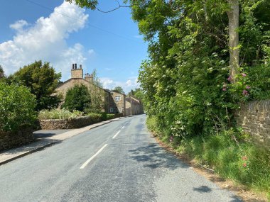 Grange Yolu 'na bakıyorum. Ağaçlar, kulübeler ve mavi gökyüzü var. Farnhill, Keighley, İngiltere.