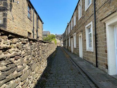 Arka sokakta taş kaldırımlar, eski kulübeler ve parlak mavi bir gökyüzü var. 