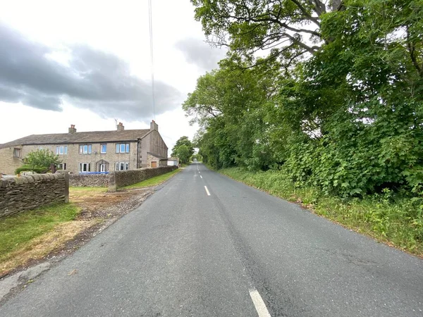 Glusburn, Keighley, İngiltere 'de bulutlu bir günde Lothersdale Yolu' nda eski binaların ve eski ağaçların yanından geçiyoruz.