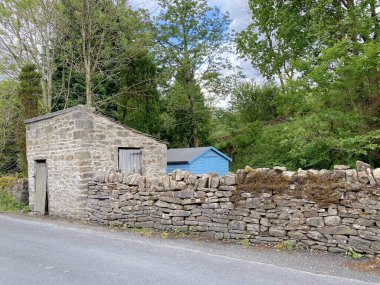 Kuru bir taş duvar, taştan bir ek bina ve arkasında eski ağaçlar olan mavi bir ahşap kulübe, Lothersdale, Keighley, İngiltere