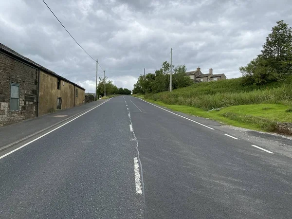 Karanlık ve bulutlu bir günde, Denshaw, Oldham, İngiltere 'de evleri ve ağaçları olan Ripponden Yolu' nu izleyin.