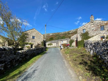 Hawkswick 'e yaklaşan yol, kurumuş taş duvarlar, kulübeler ve mavi gökyüzü ile Hawkswick, Skipton, İngiltere' de bir yaz günü.