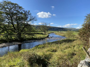 Skirfare Nehri, Hawkswick köyünü yavaşça geçerek, yabani bitkiler, eski ağaçlar ve uzak tepelerle