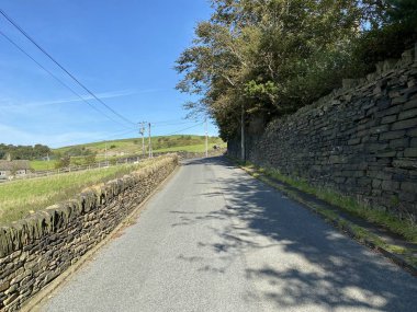 Kuru taş duvarları, ağaçları ve çiftlikleri olan Brow Lane 'e bakıyorum, Halifax, Yorkshire, İngiltere' de mavi gökyüzüne karşı.