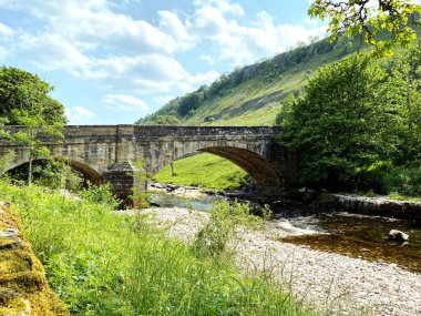 Eski taş köprü, Wharfe nehri boyunca taşlarla ve çimenli bankalarla Kettlewell, Skipton, İngiltere