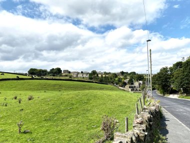 Denholme 'a uzanan Brighouse Yolu' nun kuru bir taş duvarına bakın. Tarlaları, evleri ve ağaçları var.