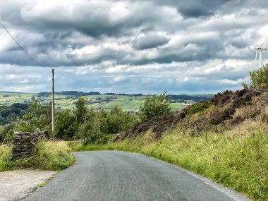 Kara Mağribi Yolu, Haworth yakınlarındaki fundalıklara doğru gidiyor. Uzakta, Haworth, Keighley, İngiltere 'de yoğun bulut ve tarlalar var.