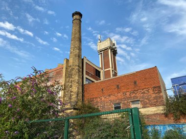 Victoria dönemi bacası, Bradford, Yorkshire, İngiltere 'de mavi gökyüzüne karşı duran eski bir kırmızı tuğla binanın yanında duruyordu.