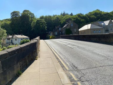 Nehir üzerinden geçen eski taş köprü, Bingley, Bradford, İngiltere 'deki evler ve eski ağaçlarla birlikte.