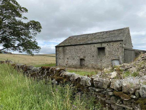 Old stone barn, in a field next to a dry stone wall, and long grass near, Malham, Skipton, UK