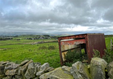 Allerton, Bradford, İngiltere 'de yağmurlu bir günde, Aire Vadisi' nin olduğu kuru bir taş duvarın yanında paslı bir konteynır.