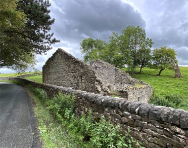 Eski taş harabe, kuru bir taş duvarın yanında, yakınlarda ağaçlar ve tepeler, Airton, Skipton, İngiltere.