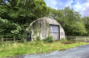 B6451 yolu, Leathley, Otley, İngiltere 'nin yakınındaki ağaçlarla ve ahşap çitlerle çevrili yarı dairesel eski kulübe.