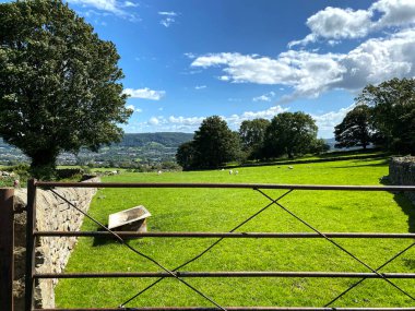 Eski bir su küveti, kuru bir taş duvar ve Newall 'da Clifton, Otley, İngiltere ile birlikte uzak tepeleri olan metal bir çiftlik kapısına bakıyorum.