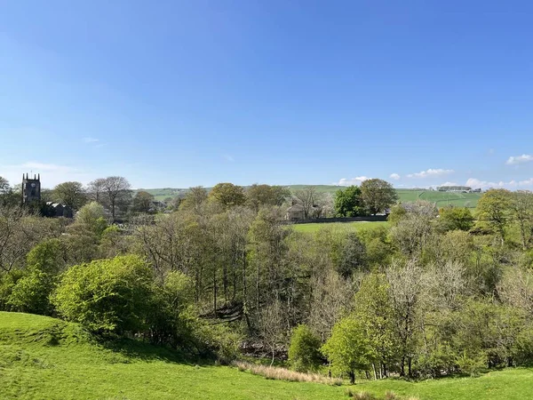 Geniş bir manzara, ağaçlar, dere tepeleri ve Cowling, Keighley, İngiltere 'deki Kutsal Üçlemeci Kilisesi.