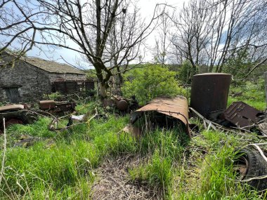 Paslı tarım makineleri, aşırı gelişmiş bir arazide, Stainforth, Settle, İngiltere yakınlarındaki eski bir taş binanın yakınında.