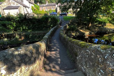 View over an old stone bridge, spanning the, Clapham Beck, with old trees, and cottages in, Clapham, UK
