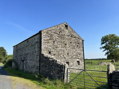 Old stone barn, with a farm gate and fields, on a hot day on, Holm Lane, Austwick, UK