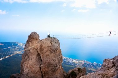 A majestic view of the high rope bridge with the traveler over the abyss on the Black Sea coast.