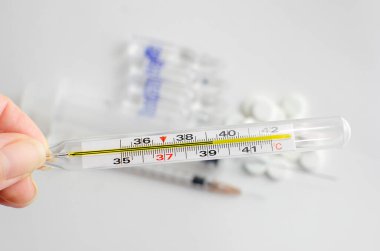 El, yüksek ateş gösteren bir civa tıbbi termometre tutuyor. Uyuşturuculu beyaz arkaplan.