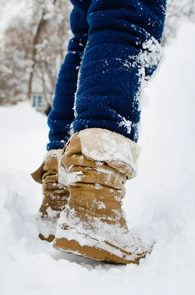 Karlı bir yolda yürüyen bir kadın. Bacaklar botların içinde, yakın plan. Dikey fotoğrafçılık.