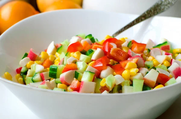 Taze sebze salatası - salatalık, dolma biber, mısır ve yengeç çubukları masada beyaz bir kasede.