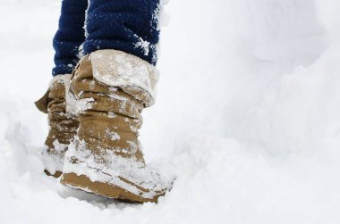 Bir insan karlı bir yolda yürür. Bacaklar botların içinde, yakın plan..