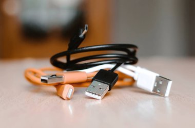 Masadaki bir cep telefonunu şarj etmek için çok renkli kablolar. Yakın çekim, seçici odaklanma.