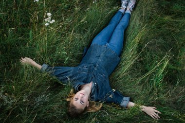 Kot takım elbiseli genç bir kız gün batımında çayırda uzanıyor.