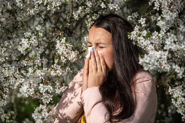 Concepto de síntomas de alergia de primavera, mujer joven estornudando frente a la floración de un árbol, alergia al polen y la temporada de floración, atención médica — Foto de Stock