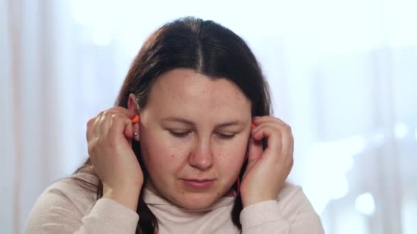 Young woman suffering of tinnitus disease, putting on her earplugs, insomnia or stress concept, sick female having an ear pain touching her painful head, healthcare — Stock Video