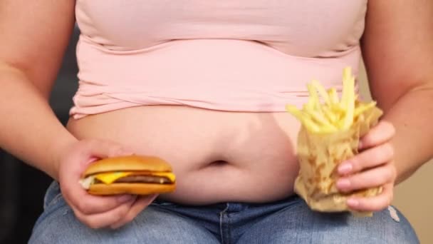 Mujer joven con sobrepeso o más tamaño con grasa, vientre grande y comida poco saludable hamburguesa y papas fritas, vida de un pueblo xl tamaño, concepto grueso y gordo — Vídeos de Stock