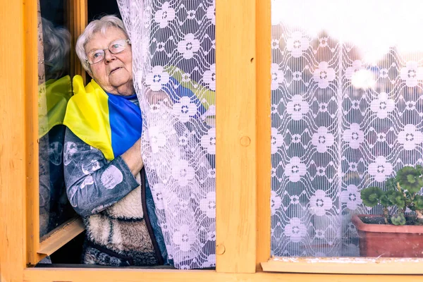 Mujer mayor mirando por la ventana y mirando a la agresión rusa en Ucrania, conflicto de guerra, rezar por Ucrania — Foto de Stock