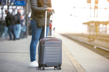 El bagajlı genç bir kadın tren istasyonunda tren bekliyor, ulaşım konsepti.