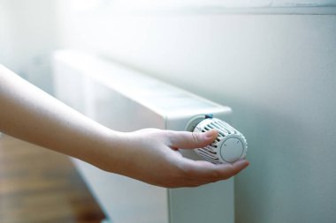 Woman hand regulates a temperature on the radiator, high electricity and gas prices, economic crisis