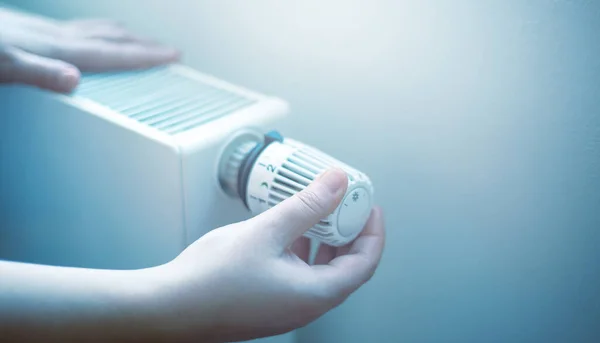 Woman hand regulates a temperature on the radiator, high electricity and gas prices, economic crisis