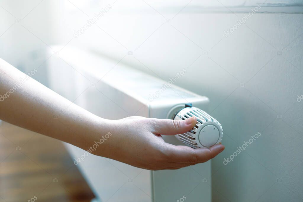 Woman hand regulates a temperature on the radiator, high electricity and gas prices, economic crisis