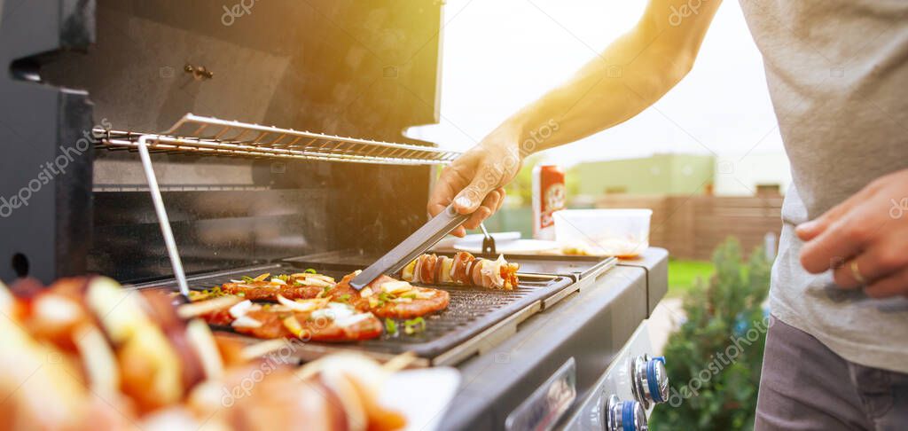 Young man grilling some kind of meats on a gas grill during lovely summer time, food concept