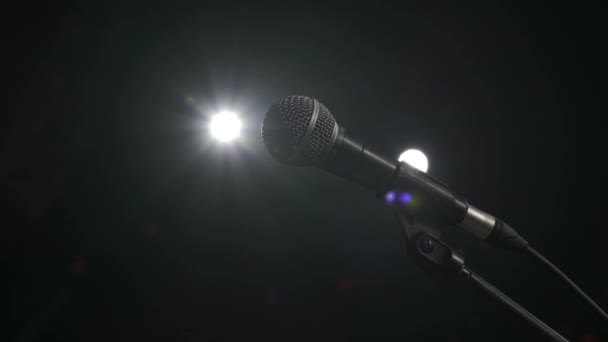 Professzionális mikrofon üres sötét színpadon, fekete háttérrel. Fénysugarak, emberek nélkül. — Stock videók