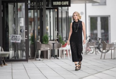 Litvanya 'daki Vilnius Old Town Caddesi. Beyaz, beyaz, yetişkin bir kadın siyah elbise ve boynuna bijouterie giyiyor. Dışarıdaki Sandalyelerle Arka planda Dükkan ve Restoran