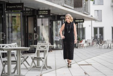 Litvanya 'daki Vilnius Old Town Caddesi. Beyaz, beyaz, yetişkin bir kadın siyah elbise ve boynuna bijouterie giyiyor. Dışarıdaki Sandalyelerle Arka planda Dükkan ve Restoran