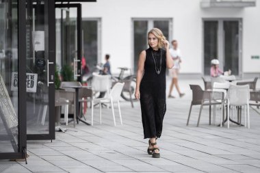 Litvanya 'daki Vilnius Old Town Caddesi. Beyaz, beyaz, yetişkin bir kadın siyah elbise ve boynuna bijouterie giyiyor. Dışarıdaki Sandalyelerle Arka planda Dükkan ve Restoran