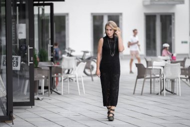 Litvanya 'daki Vilnius Old Town Caddesi. Beyaz, beyaz, yetişkin bir kadın siyah elbise ve boynuna bijouterie giyiyor. Dışarıdaki Sandalyelerle Arka planda Dükkan ve Restoran