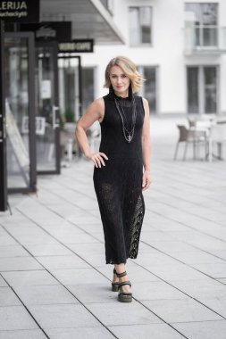 Litvanya 'daki Vilnius Old Town Caddesi. Beyaz, beyaz, yetişkin bir kadın siyah elbise ve boynuna bijouterie giyiyor. Dışarıdaki Sandalyelerle Arka planda Dükkan ve Restoran