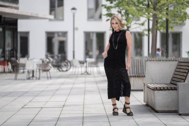Litvanya 'daki Vilnius Old Town Caddesi. Beyaz, beyaz, yetişkin bir kadın siyah elbise ve boynuna bijouterie giyiyor. Dışarıdaki Sandalyelerle Arka planda Dükkan ve Restoran