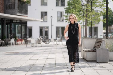 Litvanya 'daki Vilnius Old Town Caddesi. Beyaz, beyaz, yetişkin bir kadın siyah elbise ve boynuna bijouterie giyiyor. Dışarıdaki Sandalyelerle Arka planda Dükkan ve Restoran